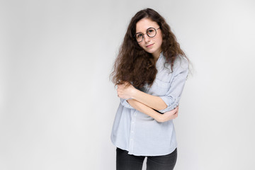Portrait of a young girl in glasses. Beautiful young girl on a gray background. The girl is holding glasses in her hands. The girl folded her arms.