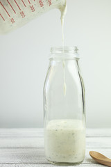 Homemade yogurt salad dressing being poured into a milk bottle