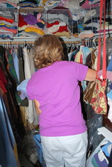 Mature female blond beauty looking for a blouse in her crowded closet.