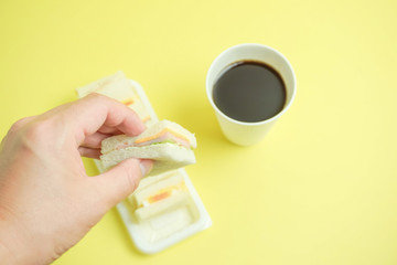  The photograph which eats a sandwich.  サンドウィッチを食べる写真　　A hand to pick up a sandwich and the coffee which were ready in a paper cup.  サンドウィッチを取る手と紙コップに入ったコーヒー
