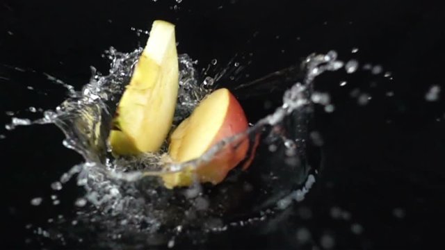 Super Slow Motion of Sliced Apple Falling with Water Splash on Black Surface