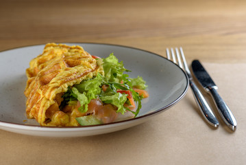 Omelette with mushrooms and salad. Home omelette with fried mushrooms, salmon, fresh leaves of Iceberg on a plate and vintage wooden table. Stuffed vegetarian omelette idea. Rustic style