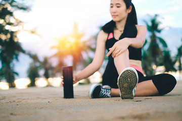 Asia beautiful woman in sport ware sitting on the beach and drinking water after exercise. 