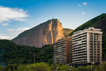 Fototapeta na wymiar Luxury Condominium Buildings Between Green Hills in Rio de Janeiro and Corcovado Mountain Lit by Sunlight by Sunrise
