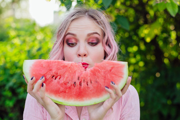 Beautiful young woman with pink hair enjoying watermelon