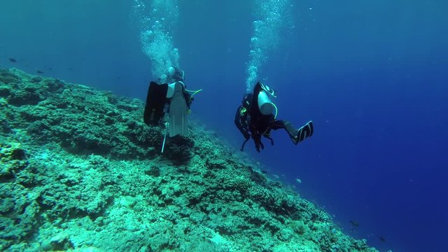 Three scuba diver sail over the slope of a coral reef in the blue water, Indian Ocean, Fuvahmulah island, Maldives
