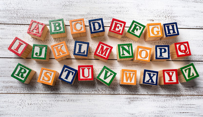 Multi-colored wooden letter blocks making the alphabet on white wood background