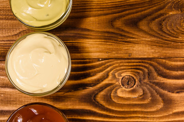 Different sauces in glass bowls on wooden table. Top view