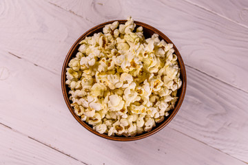 Ceramic bowl with popcorn on wooden table. Top view