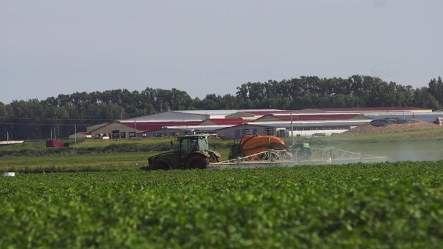 Aerial view tractor spraying the chemicals on the large green field. Spraying the herbicides on the farm land. Treatment of crops against weeds. 4K