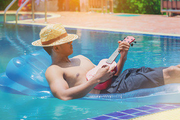 man with ukulele guitar relaxing on the air mattress in the swimming pool. vacation in summer holiday