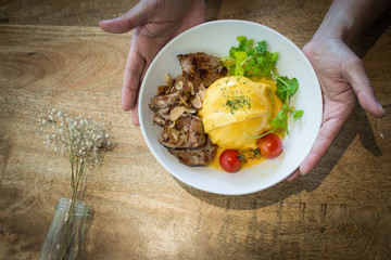 Hands serving home cooked gourmet cuisine with rustic wooden background.  Fresh organic ingredients in well balanced meal on white plate.  Copy space for text.