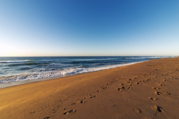 Fototapeta na wymiar Patterned Beach Sand with Footprints Coastal Blue Sky Landscape