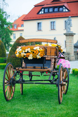 Vintage coach full of flowers on green grass outdoor. Springtime season