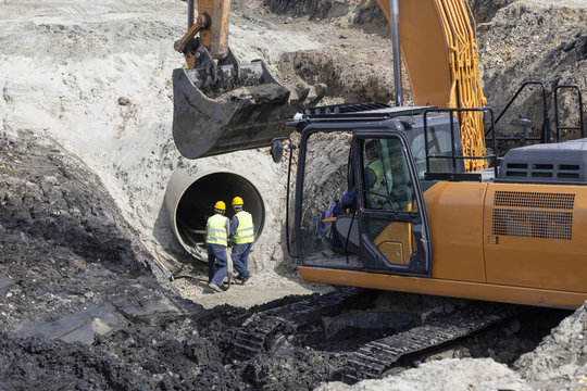 Excavator and workers making trench bed for new pipeline