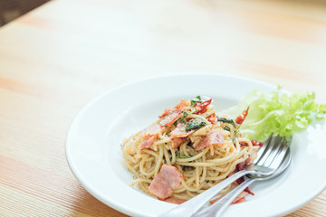 Spaghetti pasta with ham and a spoon on the table. Natural light tableware.