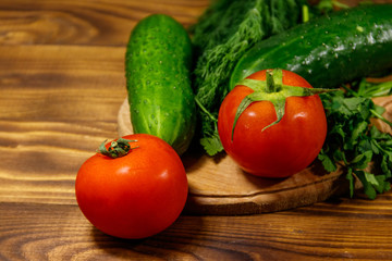 Fresh tomatoes, cucumbers, parsley and dill on cutting board on wooden table