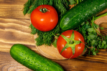 Fresh tomatoes, cucumbers, parsley and dill on cutting board on wooden table