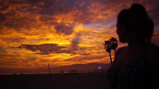 Silhouette of a young girl enjoying an orange sunset with dramatic colors in Santa Monica Beach, California.