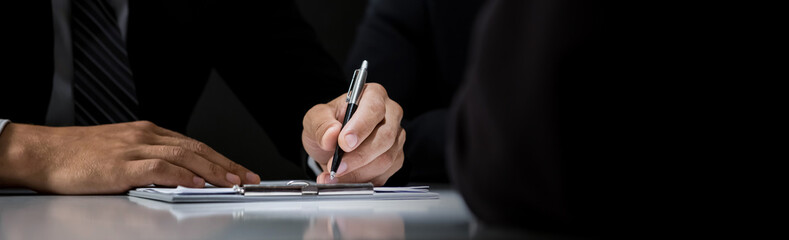 Businessman signing contract at the table in dark room, panoramic banner background with copy space