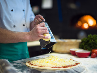 chef sprinkling cheese over fresh pizza dough