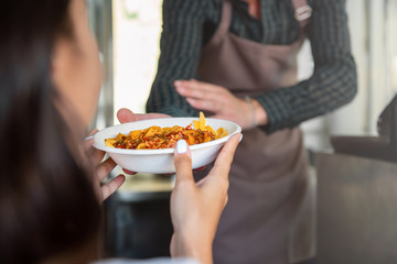 Waiter giving food, pasta in takeaway plate, to woman customer