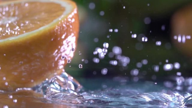 Orange hits orange juice surface and splits into halves. Slow motion shot. Close up