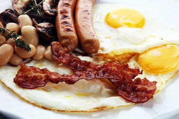 Traditional full English breakfast with fried eggs, sausages, beans, mushroomsand bacon on wooden background