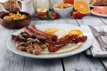 Traditional full English breakfast with fried eggs, sausages, beans, mushroomsand bacon on wooden background