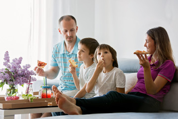 Beautiful young family with children, eating pizza at home and watching TV