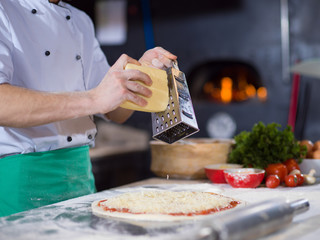 chef sprinkling cheese over fresh pizza dough