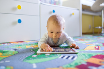 Portrait of cute little toddler child, playing on tablet, baby boy smiling