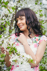 Naklejka premium Young beautiful woman enjoying smell of blooming tree on a sunny day. Outdoor portrait in a blooming spring park