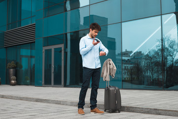 Efficient work! Smart handsome young man on business trip leaving a voice message from his cell phone and standing near the airport.