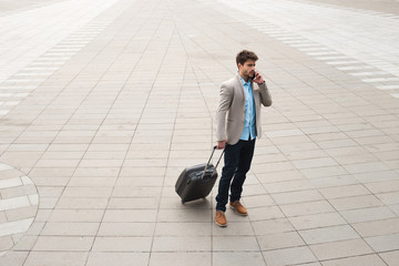 Business communication! Full body portrait of a handsome serious male business traveler walking with bag and deciding some problems by talking phone.