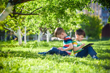 Naklejka na ściany i meble Two brother kid is lying on the grass with tablet.