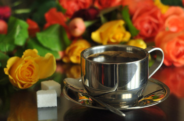 Hot coffee in a small metal cup, two pieces of sazar and multi-colored roses. Close-up.