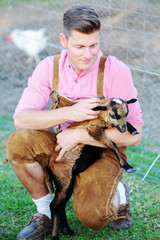 blond bavarian man holding a little goat
