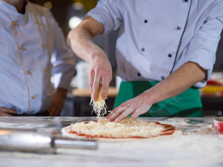 chef sprinkling cheese over fresh pizza dough