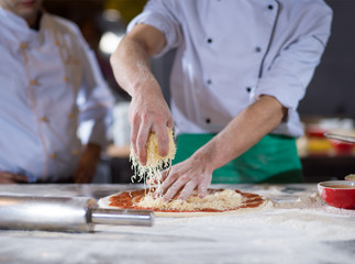 chef sprinkling cheese over fresh pizza dough