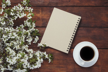 Obraz na płótnie Canvas Cup of black coffee, notepad, Sprig of cherry with flowers on dark wooden background