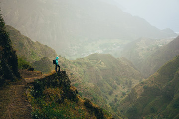 Hiker with backpack on the mountain top. Rocky terrain of a incredible panorama view of high mountain ranges and deep ravines around. Santo Antao Cape Verde