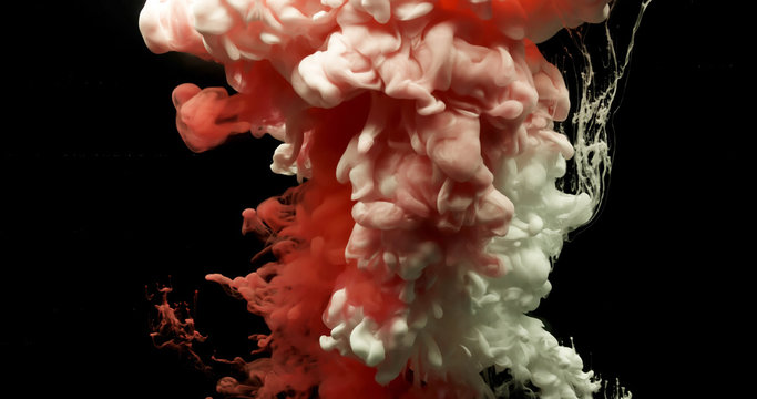 Red and white acrylic paint cloud spraying in water on black background.