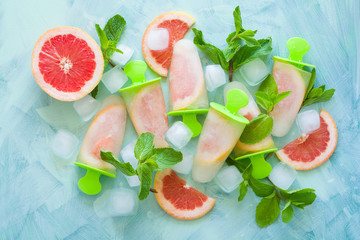 Homemade grapefruit popsicles with grapefruit slices on a mint wooden background. Top view. Copy space. Flat lay