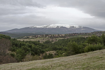 Fototapeta premium Scene with springtime mountain glade, forest, snow and residential district of bulgarian village Plana, Plana mountain, Bulgaria