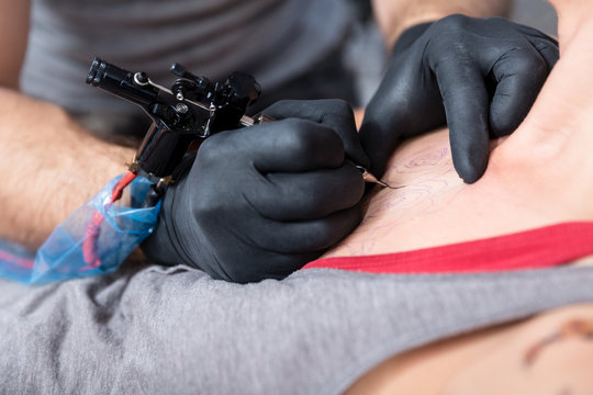 Hands of a skilled artist wearing sterile black gloves while making the contour of a new tattoo on the skin of a female client