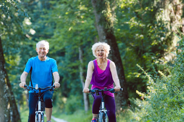 Full length of a happy and active senior couple wearing cool fitness outfits while riding bicycles...