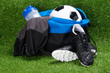 boots, soccer ball, T-shirt and a water bottle, in a sports bag, against the background of grass © kurgu128