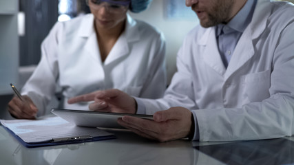 Male doctor holding tablet, giving female assistant instructions to note down