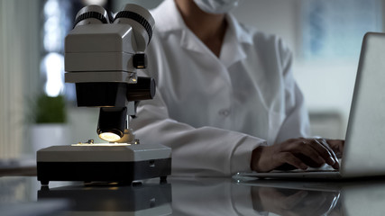 Lab worker writing observations on laptop, experiment results, clinic research